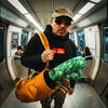 Man standing on the subway wearing Muni Kids Play Your Best Structured Snapback Hat (Camo) and Bar Logo Hoodie with Monstera Golf Headcovers