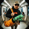 Man standing on the subway wearing Muni Kids Play Your Best Structured Snapback Hat (Camo) and Bar Logo Hoodie with Monstera Golf Headcovers